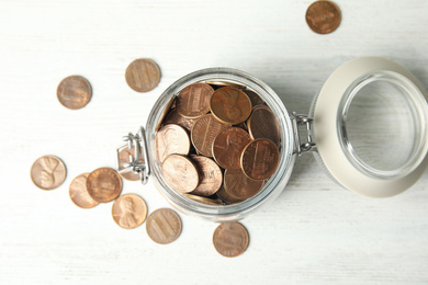 Glass jar with coins on white wooden table, flat lay