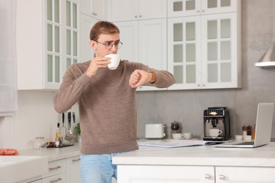 Photo of Emotional young man checking time while drinking coffee in kitchen. Being late
