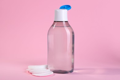 Open bottle of micellar water and cotton pads on pink background