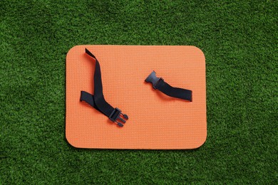 Orange foam seat mat for tourist on green grass, top view
