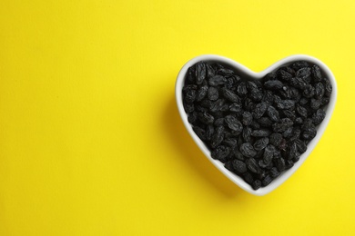 Heart shaped plate with raisins and space for text on color background, top view. Dried fruit as healthy snack