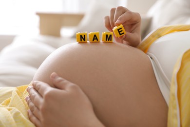 Pregnant woman with cubes on belly indoors, closeup. Choosing baby name