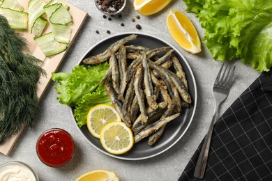 Photo of Delicious fried anchovies with lemon, lettuce leaves and sauces served on light grey table, flat lay