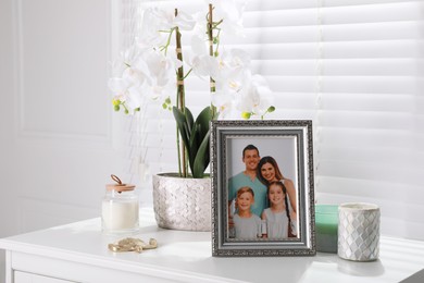 Framed family photo and orchid flower on white table indoors
