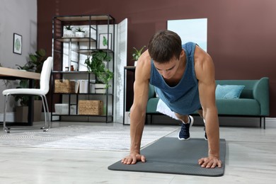 Handsome man doing high plank exercise on floor at home