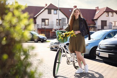 Beautiful teenage girl with bicycle and bouquet of yellow tulips outdoors on sunny day