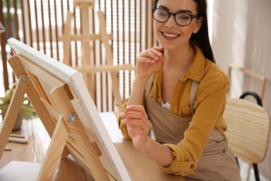 Young woman drawing on easel with pencil at table indoors