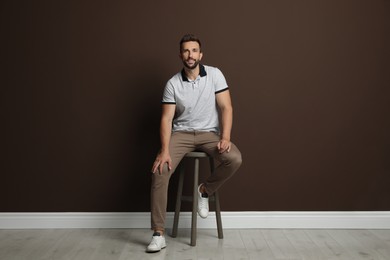 Handsome man sitting on stool near brown wall