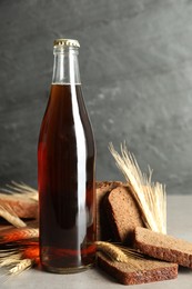Photo of Bottle of delicious fresh kvass, spikelets and bread on grey table