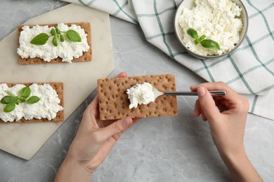 Photo of Woman spreading cottage cheese onto crispy cracker at grey marble table, top view