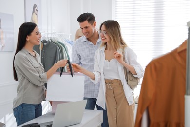 Shop assistant giving bags with clothes to couple in modern boutique