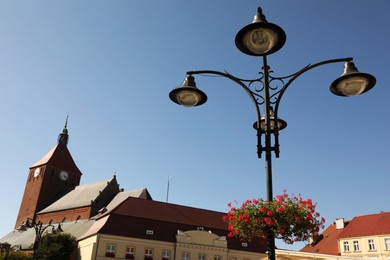 Photo of Street lamp with beautiful blooming flowers and buildings under blue sky outdoors
