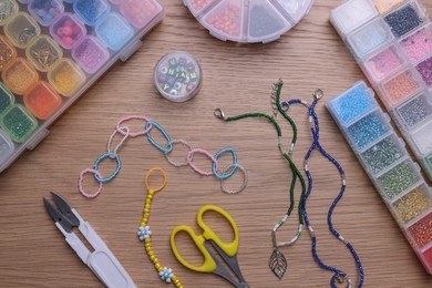 Beautiful handmade beaded jewelry and supplies on wooden table, flat lay