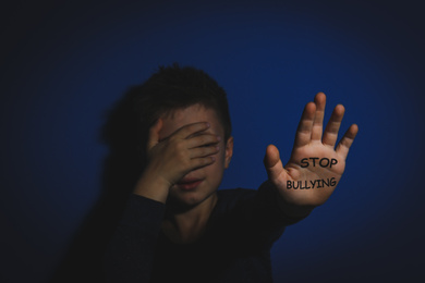 Abused little boy showing palm with message STOP BULLYING near blue wall, focus on hand