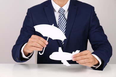 Insurance agent covering paper plane with umbrella cutout at table, closeup. Travel safety concept