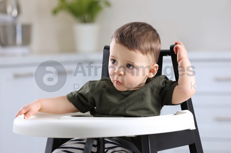 Cute little baby sitting in high chair at kitchen