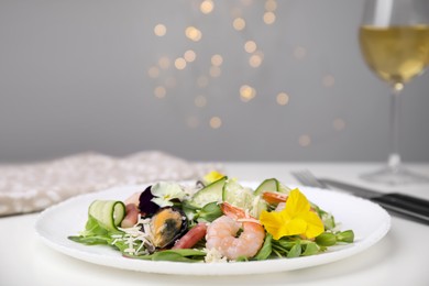 Photo of Plate of delicious salad with seafood on white table against blurred lights