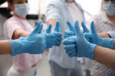Group of people in blue medical gloves showing thumbs up on blurred background, closeup