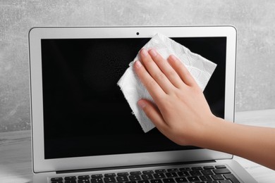 Photo of Woman wiping laptop with paper towel at white wooden table, closeup