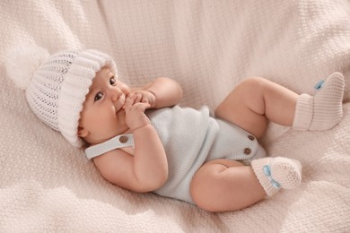 Cute little baby wearing white warm hat on knitted blanket