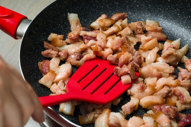 Photo of Woman cooking cracklings in frying pan, closeup. Pork lard