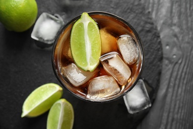 Glass of cocktail with cola, ice and cut lime on table, flat lay