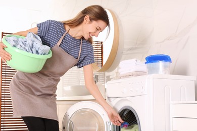 Woman putting laundry detergent capsule into washing machine indoors