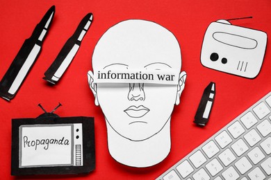 Photo of Information warfare concept. Human blinded with propaganda in media field. Flat lay composition paper cutouts and keyboard on red background