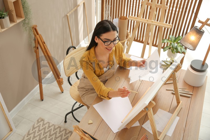 Young woman drawing on easel with pencil at table indoors, above view