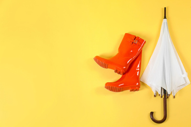 Beautiful white umbrella and red rubber boots on light yellow background, flat lay. Space for text