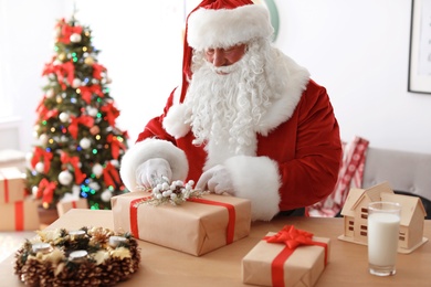 Photo of Authentic Santa Claus wrapping gift at table indoors