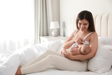 Young woman breastfeeding her little baby on bed at home