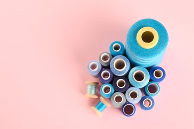 Different shades of blue sewing threads on pink background, flat lay. Space for text