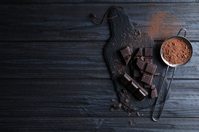 Flat lay composition with delicious dark chocolate on black wooden table. Space for text