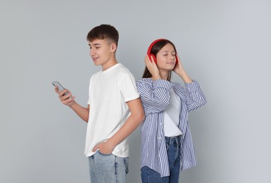Photo of Teenage boy using smartphone and girl with headphones on light grey background
