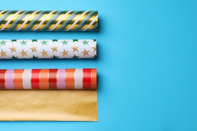 Different colorful wrapping paper rolls on light blue background, flat lay. Space for text