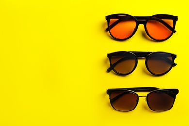 Many stylish sunglasses on yellow background, flat lay. Space for text