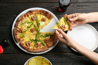 Photo of Woman taking slice of tasty cheese pizza at black wooden table, top view