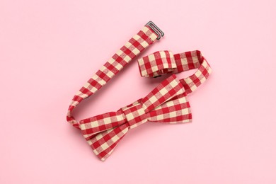 Stylish red and white gingham bow tie on pink background, top view