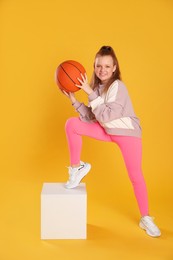 Photo of Cute indie girl with basketball ball on yellow background
