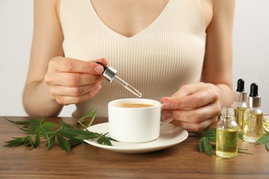 Woman dripping THC tincture or CBD oil into coffee at wooden table, closeup