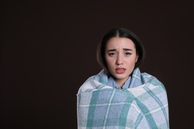 Young woman wrapped in blanket suffering from fever on dark background, space for text. Cold symptoms
