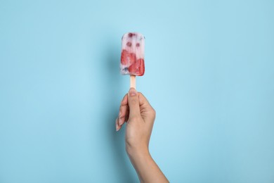 Photo of Woman holding berry popsicle on light blue background, closeup