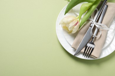 Photo of Stylish table setting with cutlery and tulip on light green background, top view. Space for text