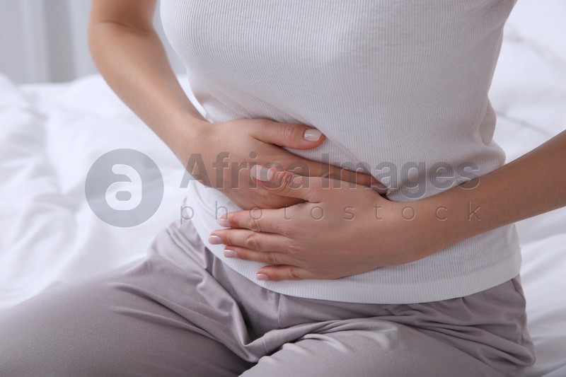 Young woman suffering from stomach ache on bed, closeup