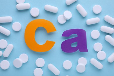Calcium symbol made of colorful letters and white pills on light blue background, flat lay