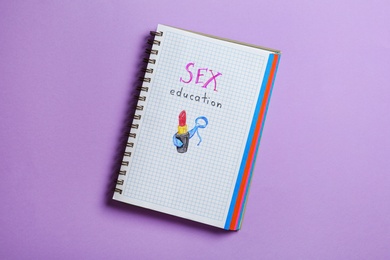 Notebook with phrase "SEX EDUCATION" on violet background, top view