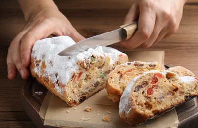 Woman cutting traditional Christmas Stollen at wooden table, closeup