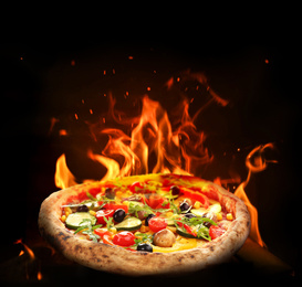 Hot tasty pizza with fire flames on dark background. Image for menu or poster