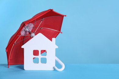 Small umbrella and house figure on light blue background. Space for text